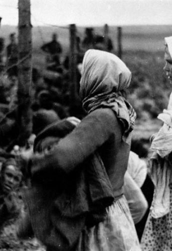 Des femmes passent des vêtements et de la nourriture aux prisonniers par-dessus le fil barbelé dans un camp de rassemblement de prisonniers de guerre. Bely (région de Kalinine). 1942. Archives de l'État russe de documents cinématographiques et photographiques (RGAKFD) / Op. 2, N° 46, sn. 22