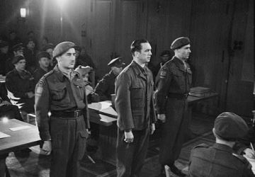 SS Brigadefuhrer Kurt Meyer standing in court with escorts Major Arthur Russel (left) and Captain Elton D. McPhail (right) in Aurich, Germany. 10 December 1945. 