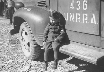 Joseph Schleifstein, survivant de Buchenwald âgé de quatre ans, est assis sur le marchepied d'un camion de l'UNRRA peu après la libération du camp. 1945. National Archives and Records Administration, College Park, Source Record ID: 111-SC-387156