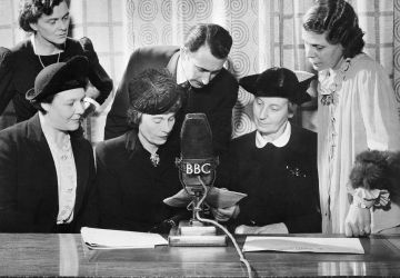 Alors que les employés hommes de la British Broadcasting Company entrent dans les forces armées, les femmes prennent à la BBC les postes de producteur, rédacteur en chef, présentateur, annonceur, créateur d’effets sonores et assurent une part importante et croissante de l’ensemble des émissions de divertissement. Personnes participant à la diffusion de la BBC à Londres, le 15 janvier 1943, pendant Answering you, émission hebdomadaire diffusée sur les ondes courtes aux États-Unis et au Canada: (de gauche à droite) Mme Mary Adams, productrice; Colin Wills, présentateur; et Mme Archer, femme au foyer et travailleuse de guerre; (assis de gauche à droite) Mme Gardner, intendante de la garderie Brook Green; Mme Margaret Biddle, épouse de l’ambassadeur américain auprès des gouvernements alliés à Londres, et Mme Florence Horsbrugh, membre du Parlement, secrétaire parlementaire du ministre de la Santé.