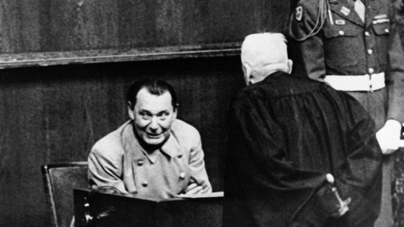 Hermann Goering smiles from the witness box as he talks with his lawyer during a recess in the war crimes trial in Nuernberg, Germany on March 15, 1946.