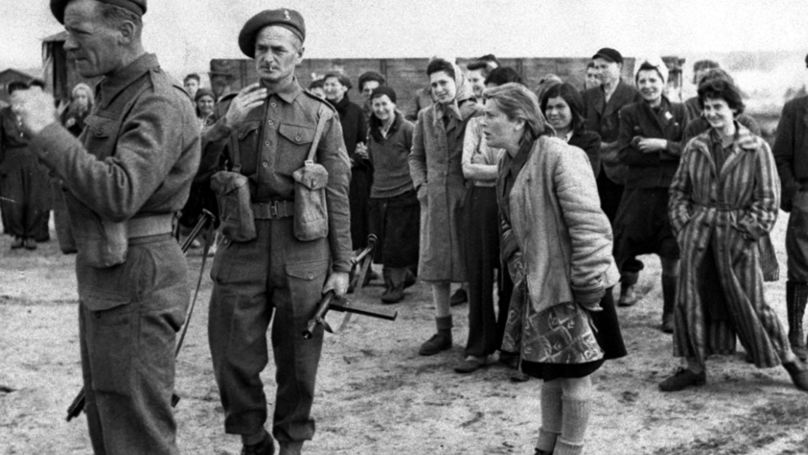 A young woman internee at the Bergen-Belsen concentration camp in Germany shouts "Shoot them, kill them as they killed our families" as Allied troops, left, supervise German POWs to clean up the camp, April 27, 1945