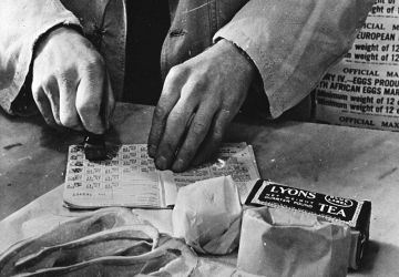 Civilian rationing: A shopkeeper cancels the coupons in a British housewife's ration book in 1943